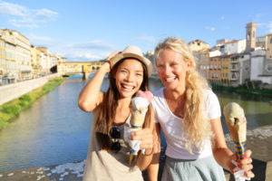 two young women in florence, italy eating gelato on the arno river with the ponte vecchio in the background