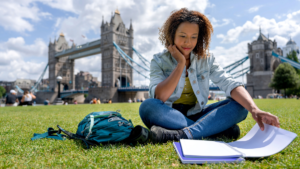 College student in London, England reading by Tower Bridge | AIFS Study Abroad
