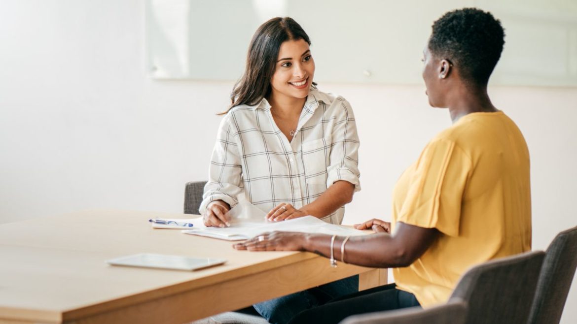 Two young professional women talking in an office setting