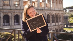Young woman with sign that says "ciao" in front of the Colosseum in Rome, Italy