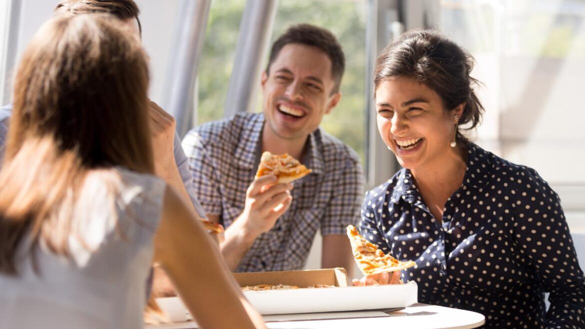 Young professional colleagues laughing and bonding over pizza at work