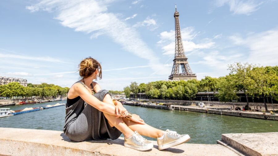 Young woman sitting in front of Eiffel Tower in Paris, France during summer