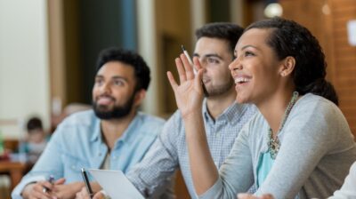 female college student raises hand in class with two male students next to her