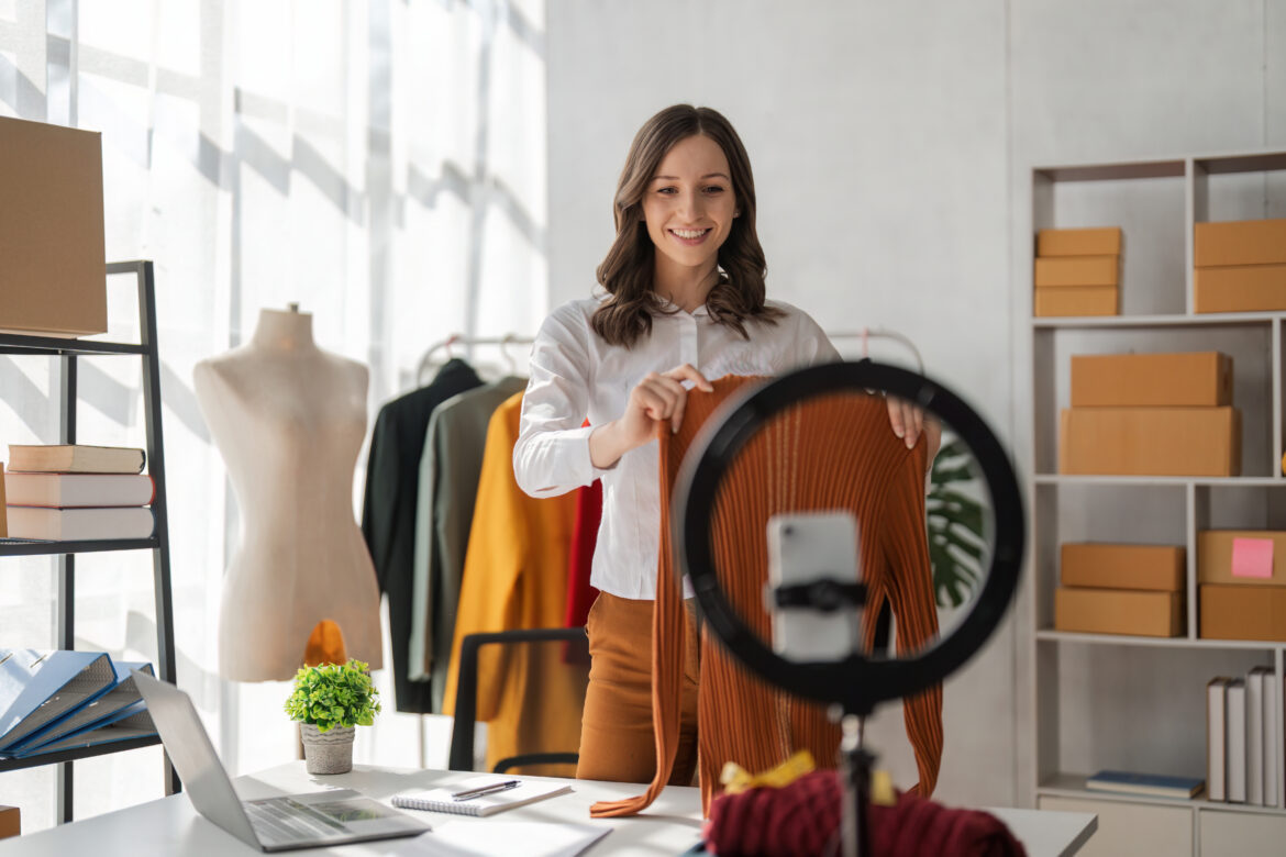 young woman fashion marketing working at home video blogging live social media presenting showing clothing products selling to customers online, video camera recording advertising marketing.